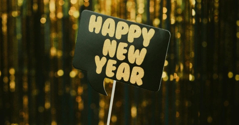 Чорна табличка з написом Happy New Year на фоні золотих блисків.