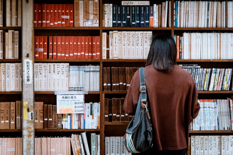 Людина читає книги в бібліотеці на полицях.